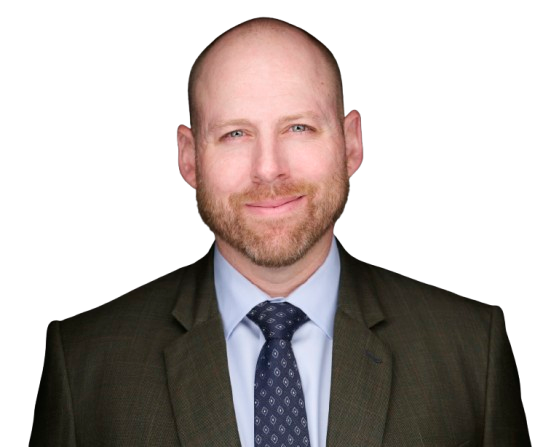 Bald man with a short beard wearing a dark suit, light blue shirt, and patterned tie, posing against a plain white background.