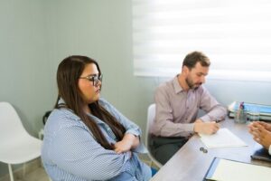 upset woman arms crossed while man signs divorce documents at desk