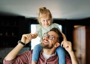 smiling father carrying young daughter on shoulders indoors during playful moment