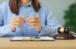 person holding wedding ring at desk beside judge gavel and legal documents