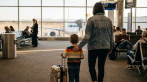 adult and young child with sticker-covered suitcase standing in airport departure gate